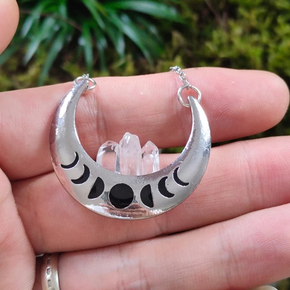 An image of the Crystal Moon Necklace, showcasing a vintage silver imitation crescent moon pendant with intricate moon phase detailing and a natural crystal transparent quartz centerpiece.