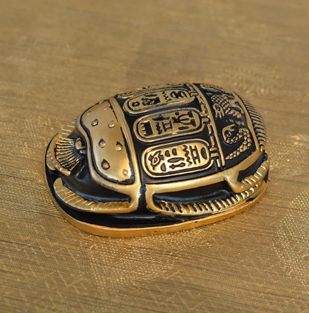 Black and gold Egyptian scarab statue adorned with hieroglyphs.